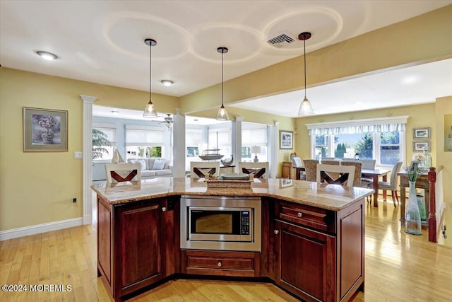 kitchen featuring stainless steel microwave, a center island, hanging light fixtures, light stone counters, and light wood-type flooring