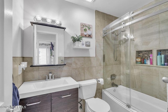 full bathroom with vanity, toilet, bath / shower combo with glass door, and tile walls