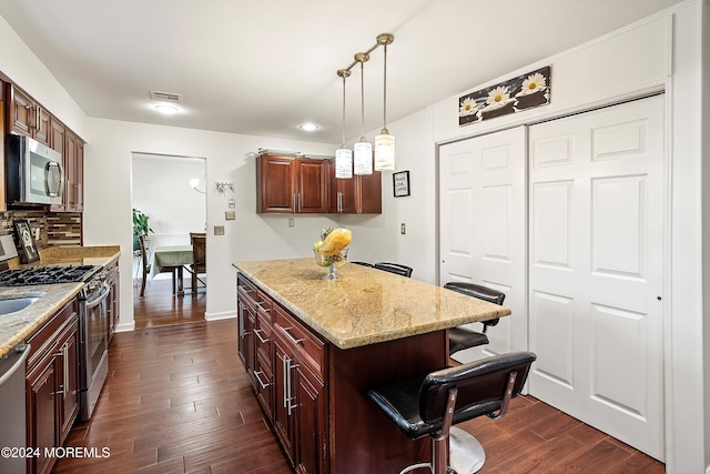 kitchen featuring appliances with stainless steel finishes, light stone counters, dark wood-type flooring, hanging light fixtures, and a breakfast bar area