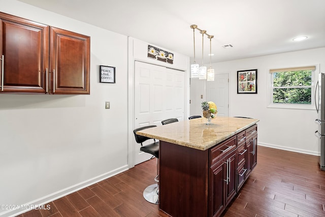 kitchen with light stone counters, stainless steel fridge, pendant lighting, a breakfast bar area, and a kitchen island