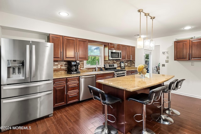 kitchen with hanging light fixtures, dark hardwood / wood-style floors, a kitchen island, light stone counters, and stainless steel appliances