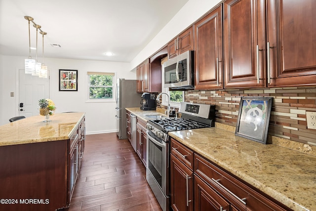 kitchen with light stone countertops, dark hardwood / wood-style flooring, stainless steel appliances, sink, and decorative light fixtures