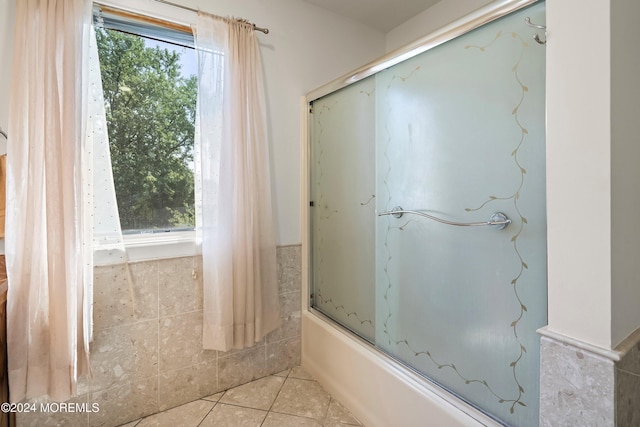 bathroom featuring tile patterned flooring, combined bath / shower with glass door, and tile walls