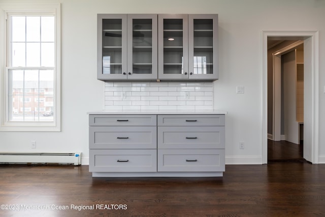 interior space featuring a healthy amount of sunlight, backsplash, a baseboard heating unit, and gray cabinetry