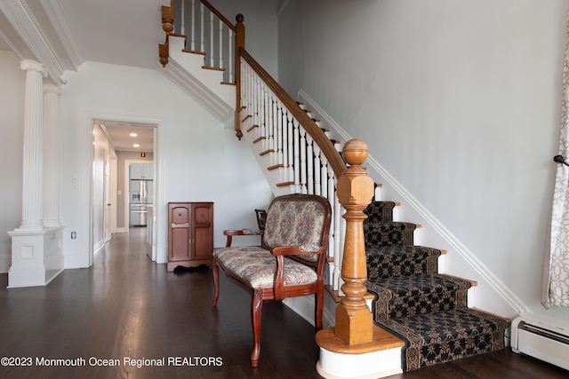 staircase featuring baseboard heating, crown molding, and decorative columns