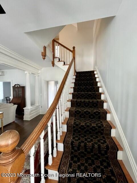 staircase with wood-type flooring, crown molding, and decorative columns