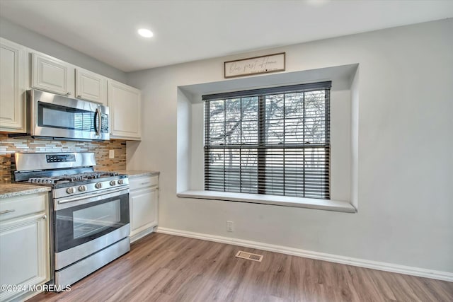 kitchen featuring white cabinetry, appliances with stainless steel finishes, light hardwood / wood-style floors, and decorative backsplash