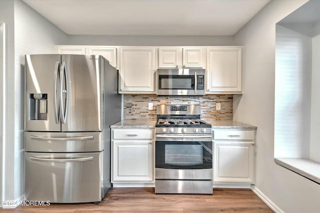 kitchen featuring white cabinetry, light stone counters, light hardwood / wood-style flooring, appliances with stainless steel finishes, and backsplash