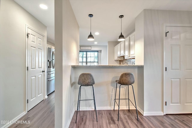 kitchen featuring a kitchen breakfast bar, tasteful backsplash, white cabinets, kitchen peninsula, and light wood-type flooring