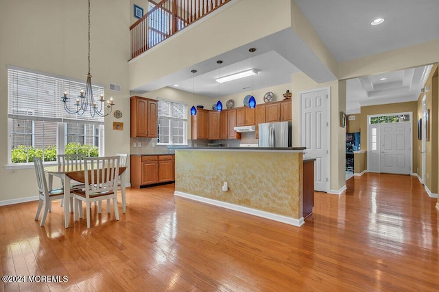 kitchen featuring pendant lighting, a healthy amount of sunlight, an inviting chandelier, a kitchen island, and stainless steel refrigerator