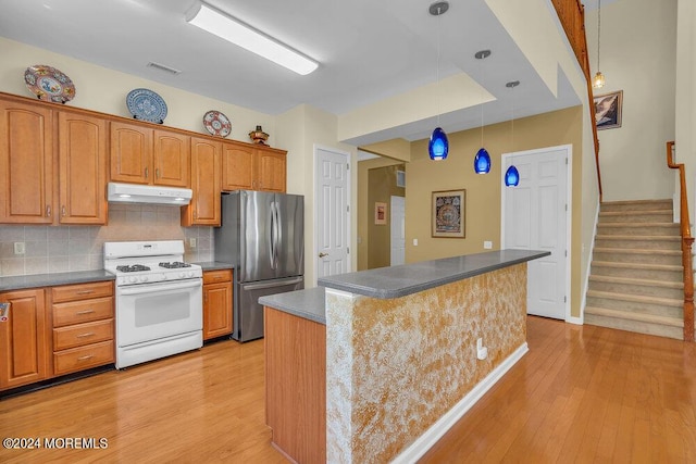 kitchen featuring stainless steel fridge, tasteful backsplash, white range with gas stovetop, a center island, and hanging light fixtures