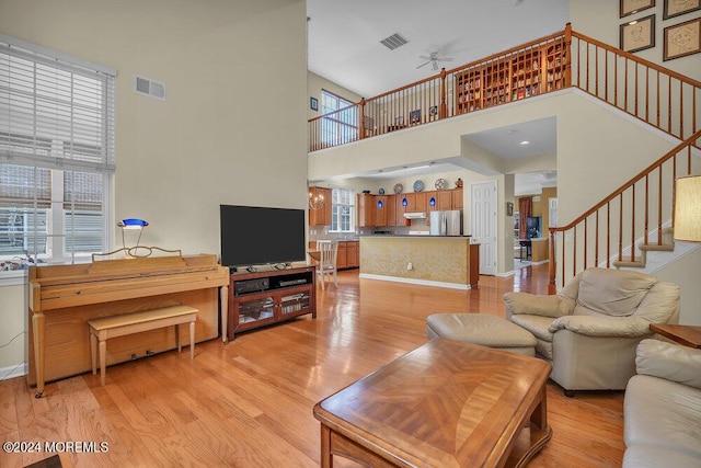 living room with light wood-type flooring, a towering ceiling, and ceiling fan