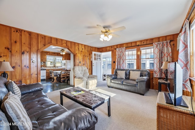 carpeted living room with a wealth of natural light, ceiling fan, and wood walls