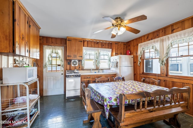 kitchen with a wealth of natural light, wood walls, ceiling fan, and white appliances