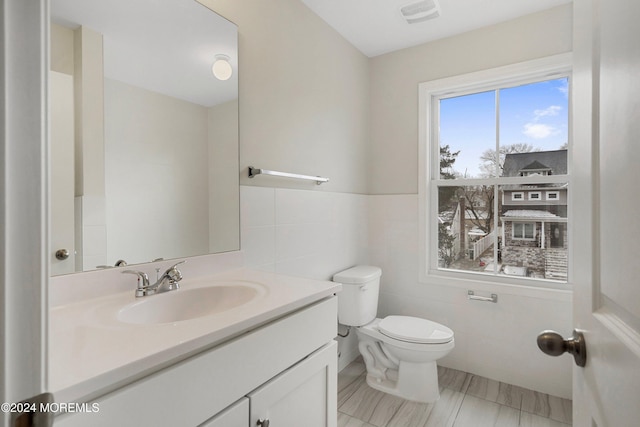 bathroom with vanity, toilet, and tile walls