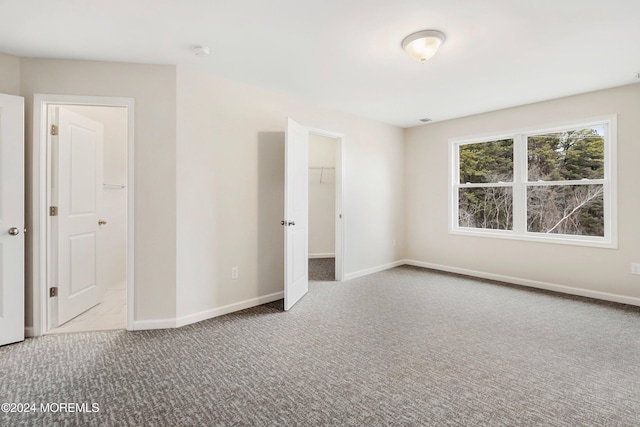 unfurnished bedroom featuring a spacious closet, a closet, and light colored carpet