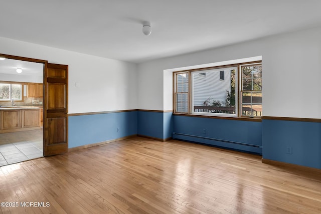 empty room featuring sink, light hardwood / wood-style flooring, and a baseboard heating unit