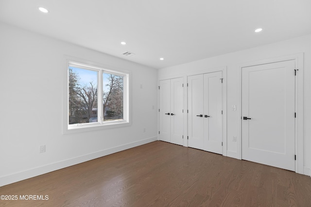 unfurnished bedroom with multiple closets and dark wood-type flooring