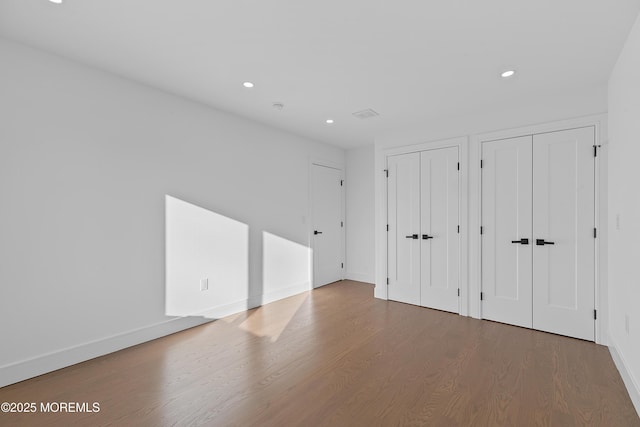 unfurnished bedroom featuring hardwood / wood-style flooring and multiple closets