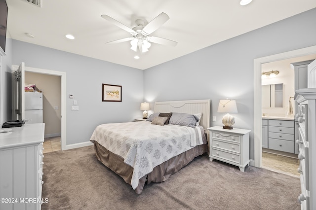 carpeted bedroom featuring white fridge, ensuite bath, and ceiling fan