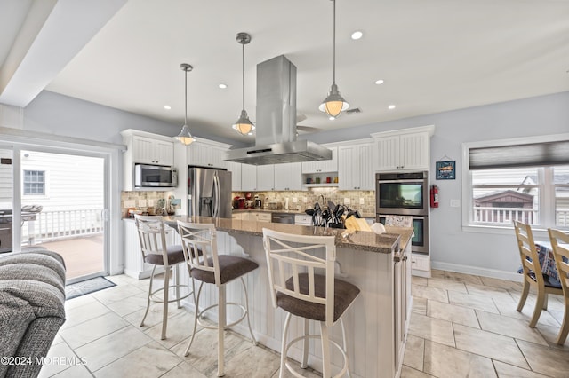 kitchen featuring light stone countertops, appliances with stainless steel finishes, decorative light fixtures, white cabinetry, and island exhaust hood