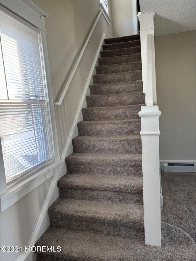 stairway featuring baseboard heating, a wealth of natural light, and carpet flooring