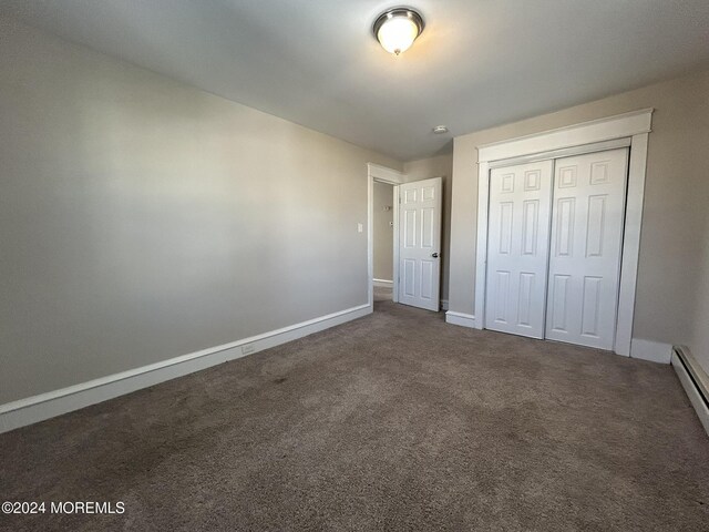 unfurnished bedroom with dark colored carpet, baseboard heating, and a closet