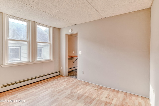 spare room with light wood-type flooring, a drop ceiling, and a baseboard heating unit