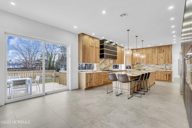 kitchen featuring a large island, light stone countertops, premium range hood, backsplash, and a breakfast bar