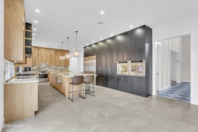 kitchen featuring appliances with stainless steel finishes, light stone counters, sink, hanging light fixtures, and a large island