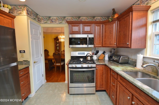 kitchen with light stone counters, stainless steel appliances, sink, an inviting chandelier, and light tile patterned flooring