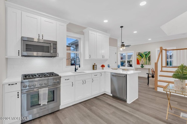 kitchen featuring kitchen peninsula, appliances with stainless steel finishes, ceiling fan, white cabinets, and light hardwood / wood-style floors