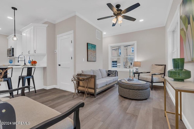 living room featuring ceiling fan, sink, wood-type flooring, and crown molding