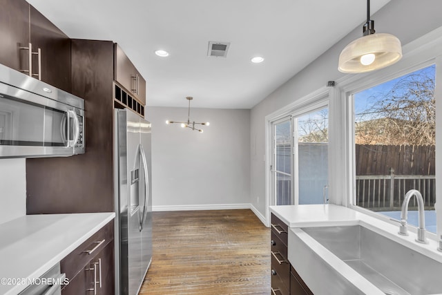 kitchen featuring appliances with stainless steel finishes, sink, pendant lighting, an inviting chandelier, and dark hardwood / wood-style floors