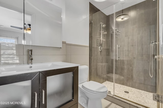 bathroom with ceiling fan, toilet, a shower with door, and tile walls