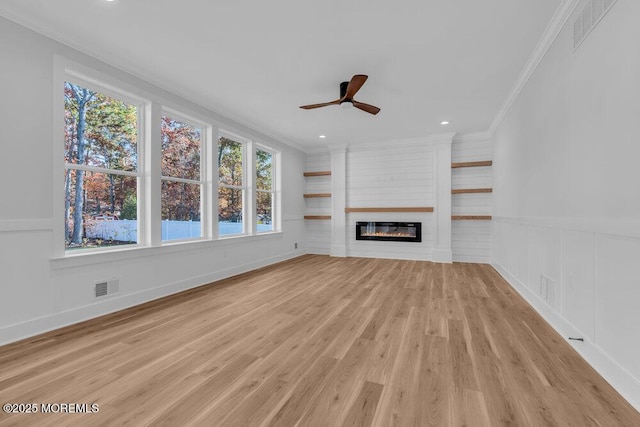 unfurnished living room featuring ceiling fan, light wood-type flooring, a large fireplace, and crown molding