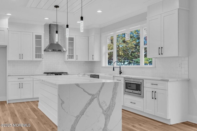 kitchen featuring stainless steel microwave, white cabinetry, wall chimney exhaust hood, and light hardwood / wood-style flooring