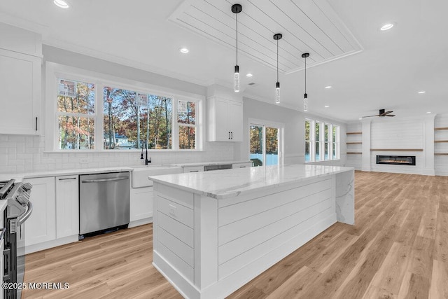 kitchen with a large fireplace, sink, white cabinetry, appliances with stainless steel finishes, and light stone counters