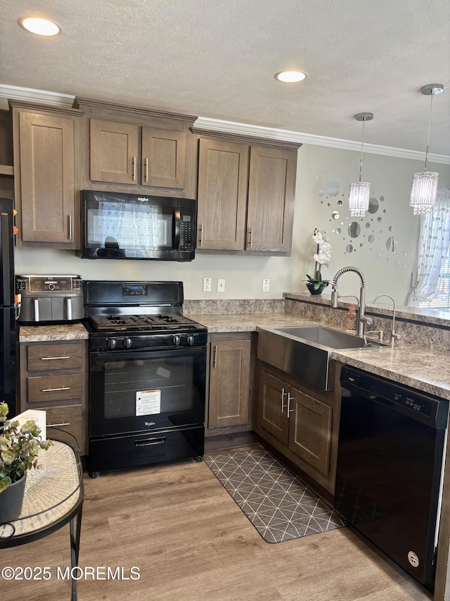 kitchen featuring pendant lighting, black appliances, light wood-type flooring, an inviting chandelier, and crown molding