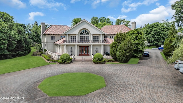 view of front facade with a front yard, french doors, a balcony, and a porch