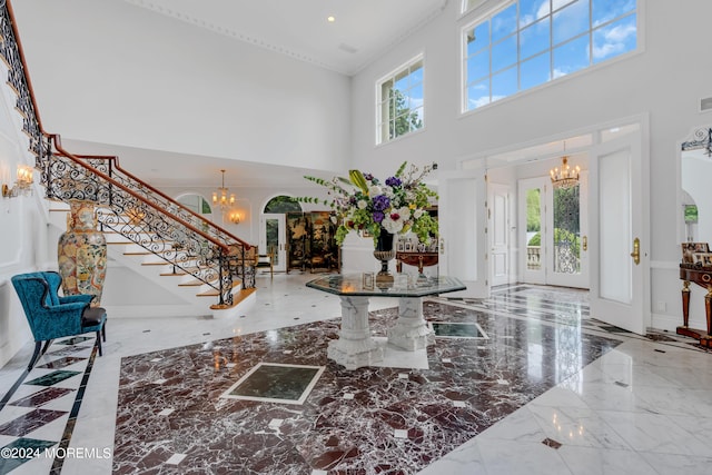 entrance foyer with french doors, a towering ceiling, an inviting chandelier, and crown molding