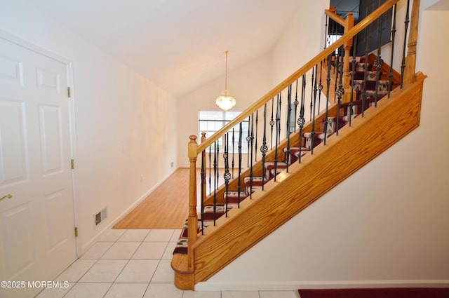 stairway with lofted ceiling, tile patterned floors, and a notable chandelier