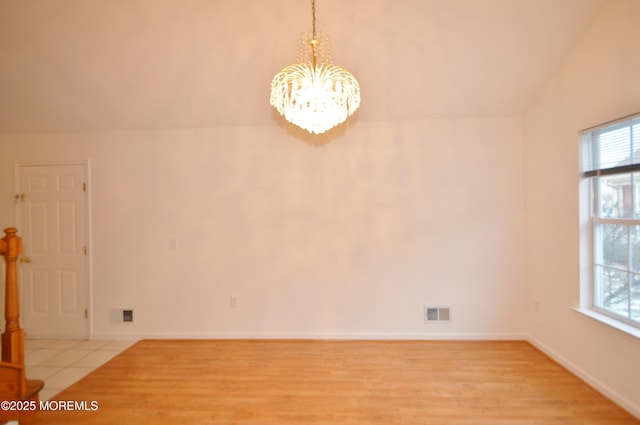 spare room with light wood-type flooring, vaulted ceiling, and an inviting chandelier