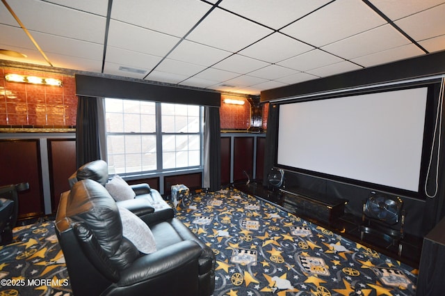 carpeted cinema room with a drop ceiling