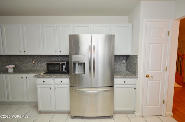 kitchen with stainless steel fridge with ice dispenser, light tile patterned flooring, and light stone countertops