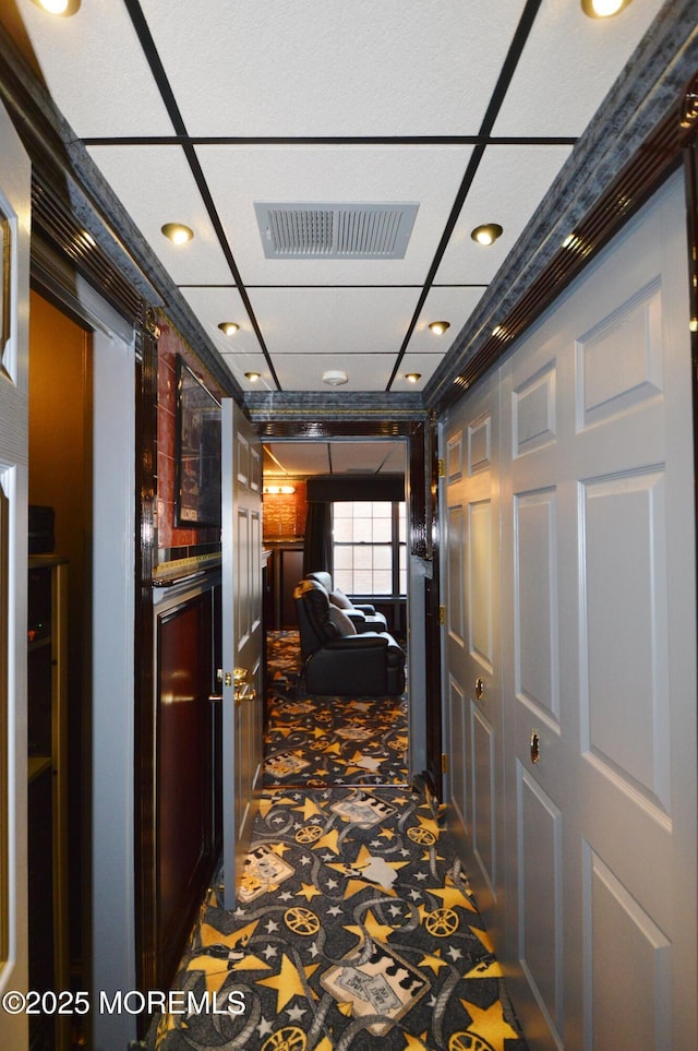 hallway with a paneled ceiling, dark carpet, and ornamental molding