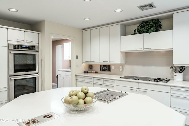 kitchen featuring white gas stovetop, stainless steel double oven, and white cabinetry