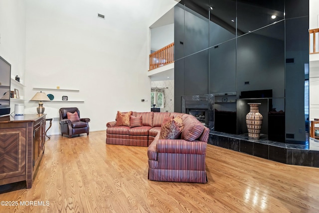 living room featuring a tiled fireplace, a high ceiling, and light wood-type flooring