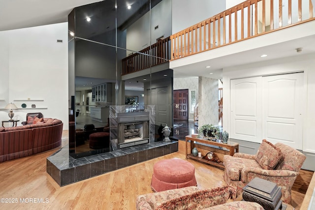 living room with wood-type flooring, a towering ceiling, and a tile fireplace