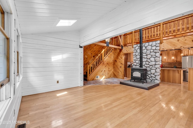 unfurnished living room featuring a wood stove, vaulted ceiling with skylight, and light wood-type flooring